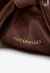 Bolsa tiracolo em couro marrom moka com laço volumoso, estilo pouch drapeado, alça com nós e fechamento por ímã. Sofisticação para qualquer ocasião!