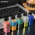 Cinco dispositivos Vaporesso Xros Cube de diferentes colores alineados sobre una superficie frente a una computadora portátil