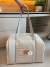 Bolsa de transporte para cachorro em tecido linen bege com alças longas, sendo segurada por uma mão em ambiente interno