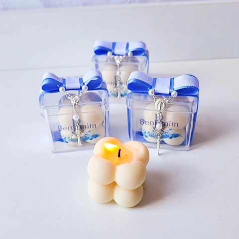 Três lembrancinhas de batizado com vela bubble acesa, embaladas em caixinhas transparentes com laços azuis.