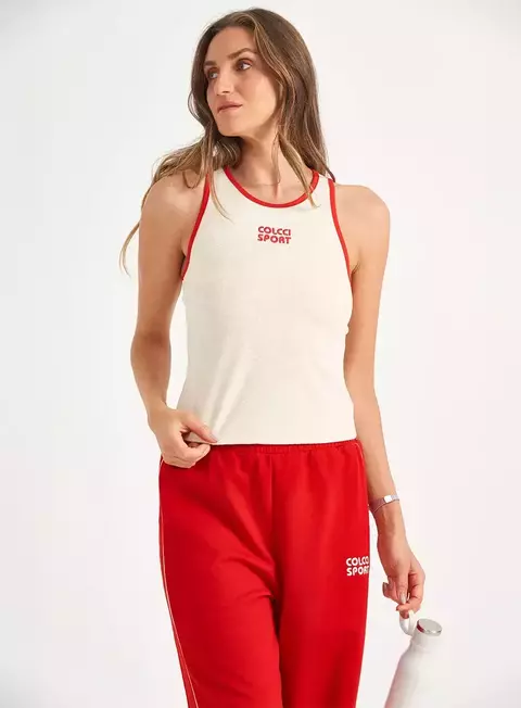 Mulher vestindo regata branca com detalhes vermelhos da marca Colcci Sport e calça esportiva vermelha, segurando garrafa branca