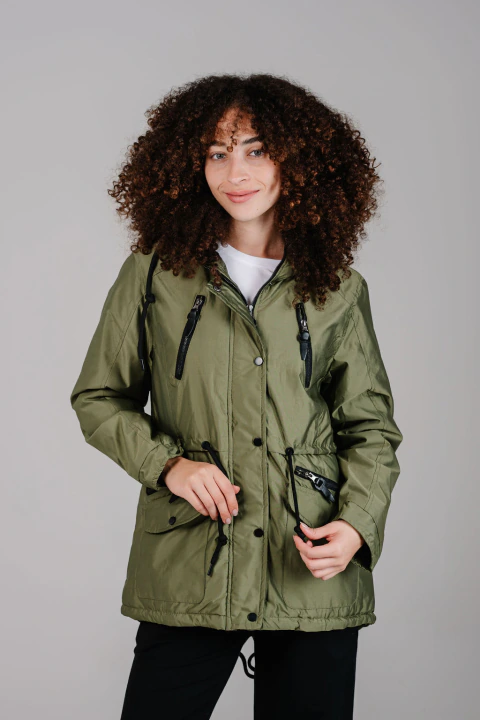 Modelo mujer con campera verde oliva Islandia, con cierre y broches delanteros, capucha fija con ajuste y bolsillos con cierres y broches