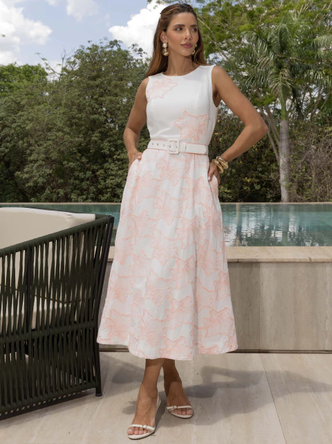 Mulher vestindo vestido de linho branco com bordado cordonnet rosa, cinto na cintura, em ambiente externo ao lado de piscina.
