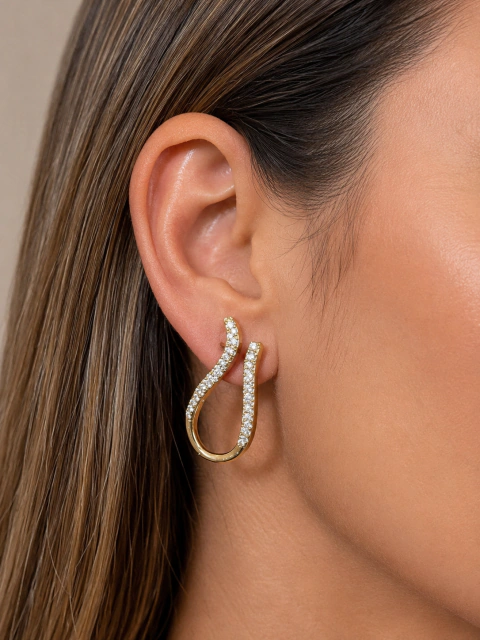 Brinco dourado elegante com design orgânico cravejado com pedras brilhantes usado em orelha feminina