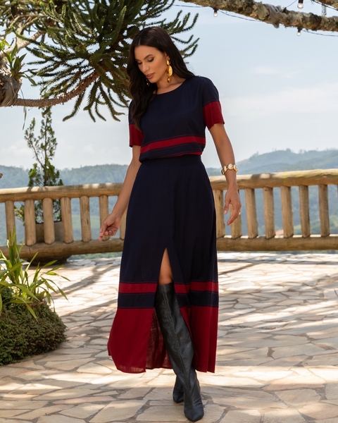 Mulher usando conjunto Denise - ART azul marinho com detalhes em vermelho, saia longa com fenda e botas pretas