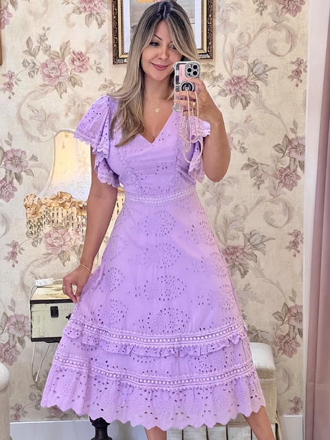 Mulher vestindo vestido midi lavanda com detalhes em bordado inglês, mangas curtas bufantes e saia com babados