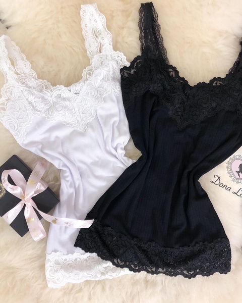 Regatas femininas Riana em branco e preto com detalhes em renda, sobre superfície clara e caixa de presente preta com laço rosa