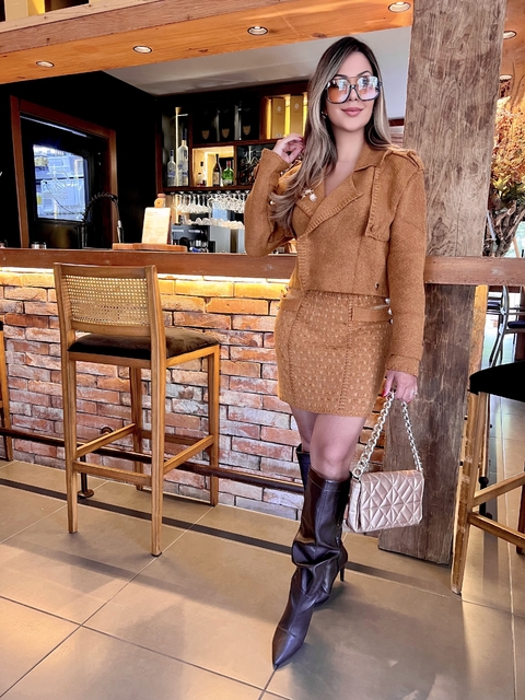Mulher vestindo saia Isabele caramelo em tricot combinada com bota marrom e bolsa bege, em ambiente de bar com decoração rústica