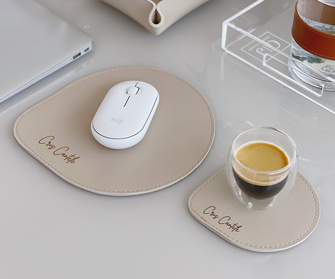 Kit de mouse pad e porta copos personalizado em tom bege sobre mesa de escritório, com mouse branco e xícara de café expresso.
