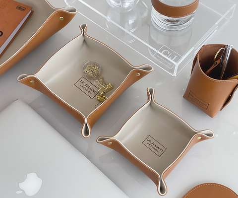 Dupla de organizadores de mesa em couro sintético personalizados, cor caramelo, usados para armazenar pequenos itens de escritório, sobre uma mesa organizada.