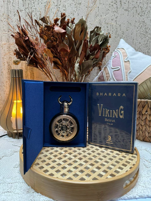 Perfume masculino Viking Beirut da marca Bharara, embalagem azul com detalhes dourados e frasco decorado com design viking, exibido sobre bandeja de madeira em ambiente decorado com flores secas e almofadas