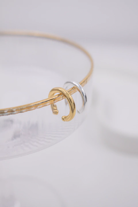 Ear cuff redondo na cor dourada e prata no fundo branco