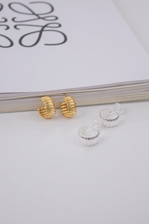 Brinco texturizado na cor dourada e prateada sobre superficie branca