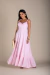Mulher usando vestido longo rosa claro com alças finas de amarrar, segurando bolsa bege