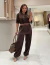 Mulher vestindo o Conjunto Isabel marrom de moda feminina, composto por blusa de manga curta, calça pantalona e cinto, em ambiente moderno de loja de roupas