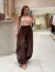 Mulher usando a Calça Tifany de renda marrom, com blusa bege de alça, em ambiente de loja de moda feminina.