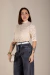 Mulher vestindo blusa Luana de renda bege com gola alta e mangas curtas, combinada com calça jeans preta e cinto branco