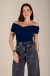 Mulher vestindo blusa azul Paola ombro a ombro com calça jeans cinza e acessórios dourados