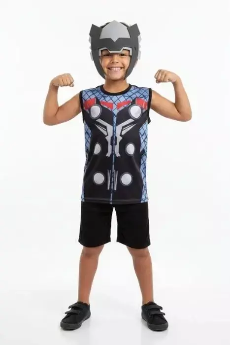 Menino sorrindo vestindo fantasia infantil do personagem Thor. O conjunto é composto por uma regata preta com estampa de armadura em tons de azul e cinza, bermuda preta lisa e uma máscara cinza em material flexível que simula o elmo do herói.