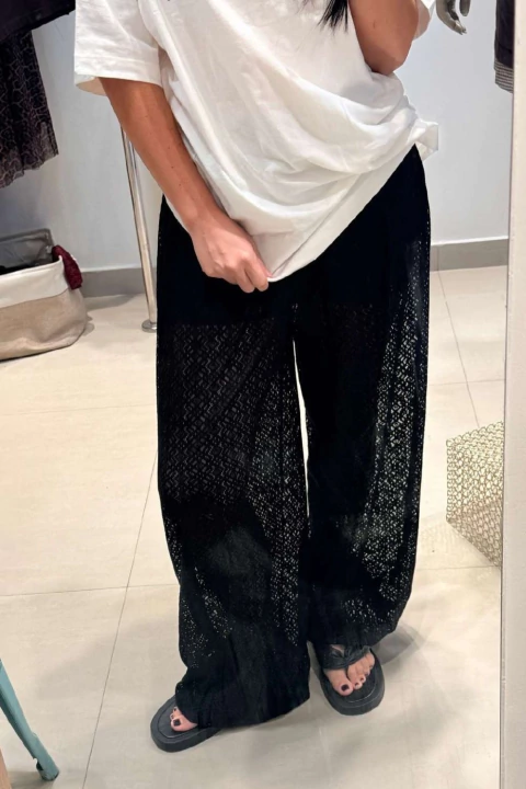 Pessoa vestindo calça bombáchá preta de renda com blusa branca, vista em frente a espelho