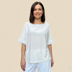 Mulher vestindo blusa branca Correnteza com detalhes em renda nas mangas e gola, combinada com calça branca texturizada