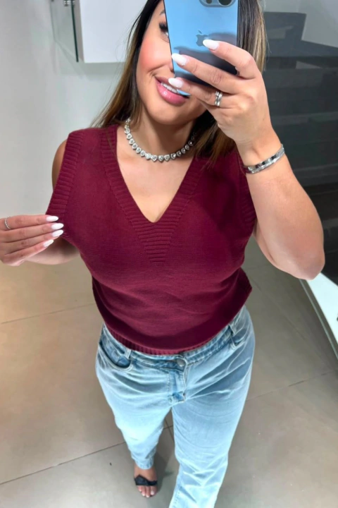 Colete feminino modal vinho com gola em V, usado com calça jeans clara e acessórios prateados, tirando selfie em espelho