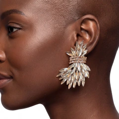 Brinco grande com pedrarias em formato de penas na cor champanhe usado por mulher negra de cabelo curto