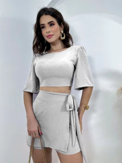 Mulher vestindo conjunto branco Duna Madri com blusa cropped de mangas curtas e saia curta com amarração lateral
