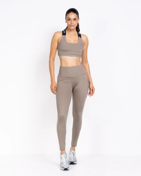 Mulher vestindo calça legging fitness com recorte e bolso lateral, combinada com top esportivo e tênis CASTANHO CANELADO


