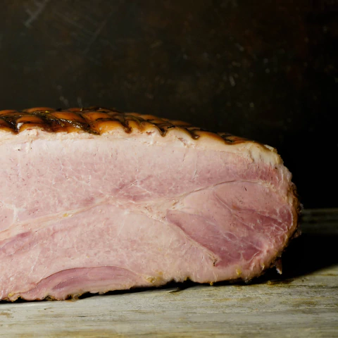 Jamón cocido asado entero con costra dorada sobre tabla de madera