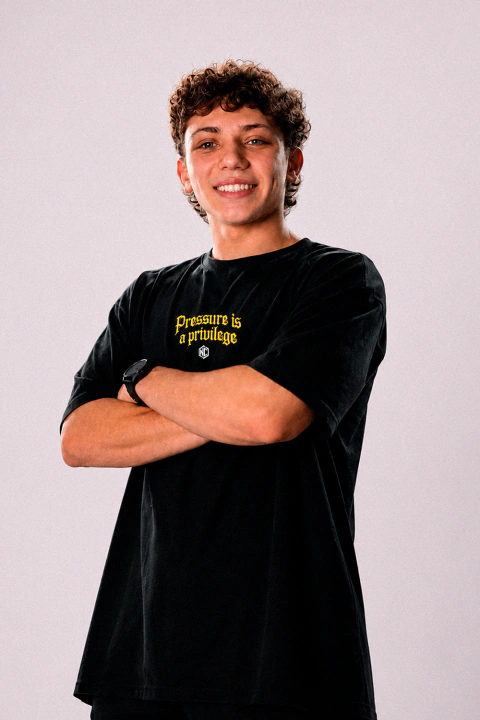 Homem jovem sorrindo usando camiseta oversized preta com estampa amarela "Pressure is a privilege"