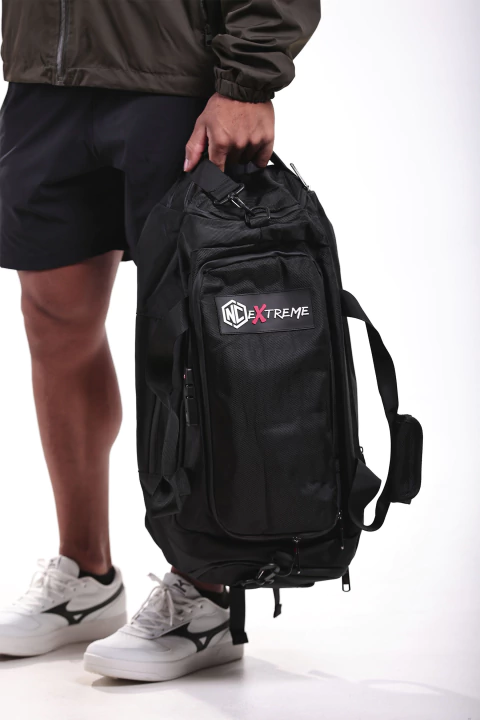 Mochila preta NC Extreme sendo segurada por uma pessoa, mostrando o logo destacado na parte frontal