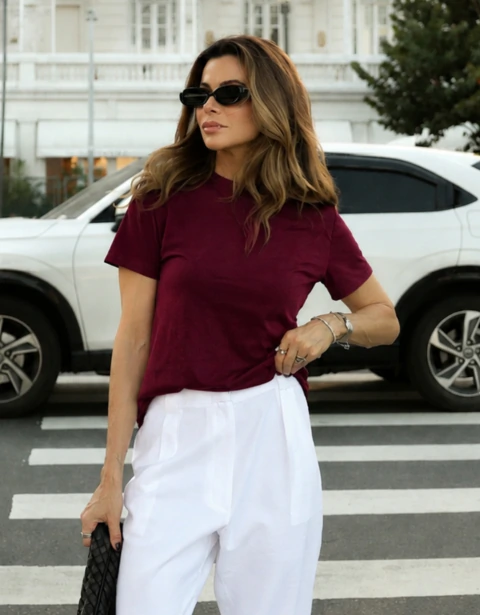 Camiseta Évora em algodão cor burgundy, com gola U e manga curta, usada por mulher em look casual com calça branca.