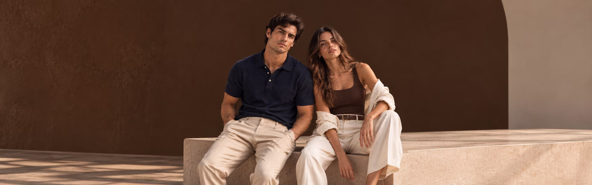 Pareja con ropa de Fratel sentada frente a una pared marrón