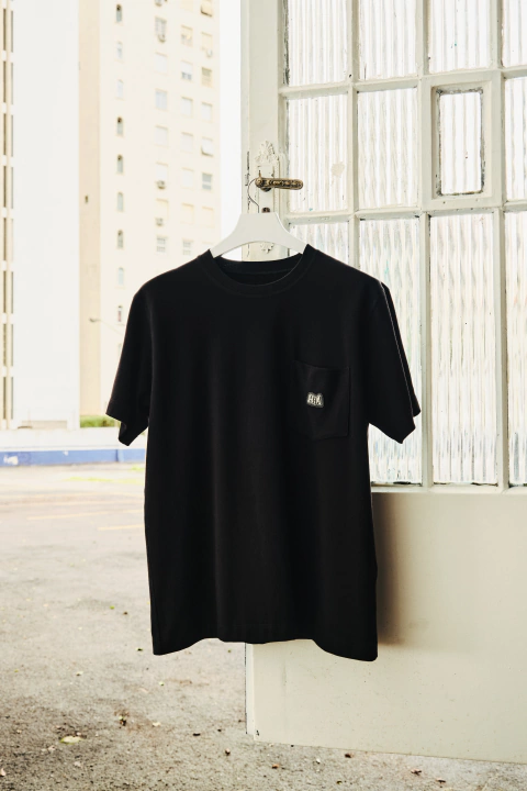Camiseta infantil preta com bolso e logo emborrachado, pendurada em cabide, destacando o design moderno da coleção I.P.26.