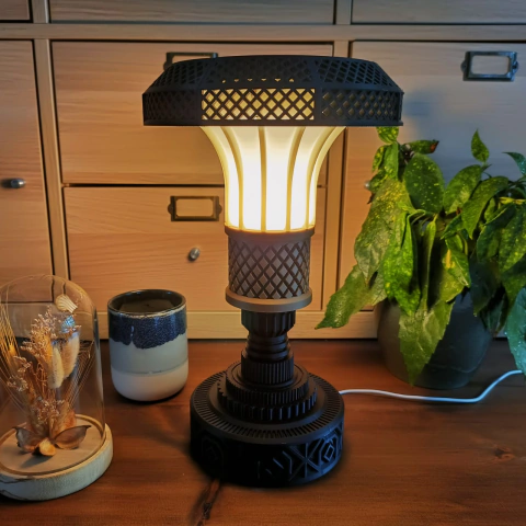 Visão frontal de uma cúpula luminária Art Déco acesa sobre uma superfície de madeira. À direita, há uma planta folhosa verde e, à esquerda, uma caneca e um objeto decorativo em uma cúpula de vidro.