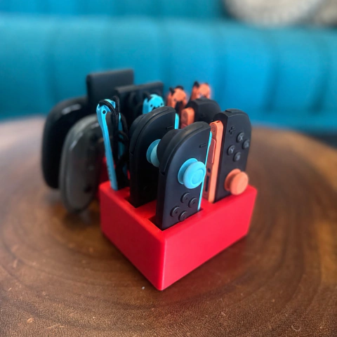 Suporte organizador gamer vermelho de mesa completamente preenchido com dois pares de controles joy-con pretos e coloridos, grips traseiros e pulseiras.