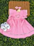 Vestido rosa bebê com bordado de coração floral, mangas com babados e laços laterais, acompanhado de faixa de cabelo e sapatinhos brancos