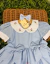 Vestido azul bebê para bebê com gola branca bordada em flores delicadas, mangas curtas com acabamento e dois laços frontais grandes