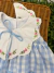 Vestido infantil Helena Xadrez Azul com gola branca bordada à mão com flores rosas e folhagens verdes, laço azul e tecido xadrez azul claro e branco