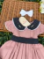 Vestido infantil rosa queimado com gola preta de poá e bordado floral, faixa preta com poá na cintura, e laço branco com pérolas
