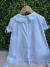 Vestido infantil branco com botões nas costas, gola arredondada com acabamento em renda, mangas bufantes com laços e barra com detalhes em renda