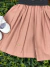 Vestido infantil rosa queimado com saia plissada, detalhes bordados na barra e faixa preta com estampa de poá na cintura, acompanhado de sapatinhos brancos