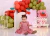 Bebê sentada usando vestido vermelho de cerejinha com babados, em festa de aniversário de 1 ano decorada com balões coloridos e luzes