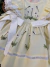 Vestido infantil amarelo claro com bordado de flores e abelhinhas, detalhes em renda nas mangas e laço branco na cintura