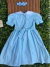 Vestido azul bebê infantil com gola peter pan branca, mangas bufantes e laço na cintura, acompanhado de uma faixa de cabelo azul