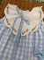 Vestido infantil Helena Xadrez com estampa xadrez azul claro e branco, gola branca bordada à mão com flores rosas e folhagens verdes, detalhe de laço azul