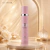 Body Splash Dalila Isabelle La Belle 300ml em frasco rosa com detalhes prateados, exibido sobre base redonda de mármore em fundo dourado elegante com rosas brancas e decoração refinada