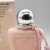 Frasco rosa claro fosco de perfume feminino com tampa prateada brilhante e cordão rosa amarrado