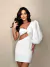 Modelo usando um vestido branco de manga balonê com detalhe de nó na frente e recorte lateral.